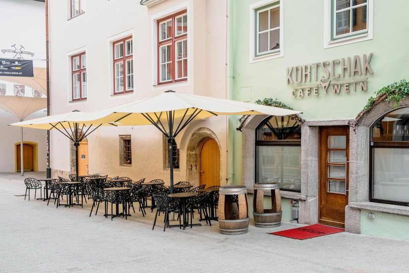 Kortschak Sommer Außenansicht des Café Kortschak mit Tischen, Stühlen und Sonnenschirmen in einer gepflasterten Gasse.