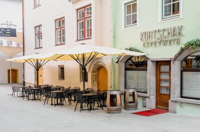 Kortschak Sommer Außenansicht des Café Kortschak mit Tischen, Stühlen und Sonnenschirmen in einer gepflasterten Gasse.