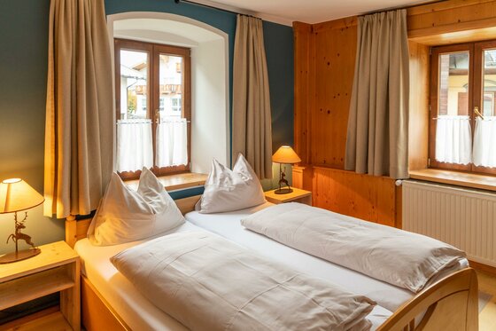 Schlafzimmer im Safestay Kitzbühel Doppelbett in einem Zimmer mit Holzvertäfelung, zwei Fenstern und Nachttischlampen.