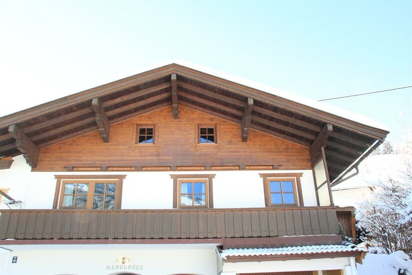 Künstlhäusl im Winter Vorderansicht eines zweistöckigen Alpenhauses mit Holzbalkon und schneebedecktem Satteldach.