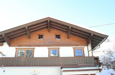 Vorderansicht eines zweistöckigen Alpenhauses mit Holzbalkon und schneebedecktem Satteldach.