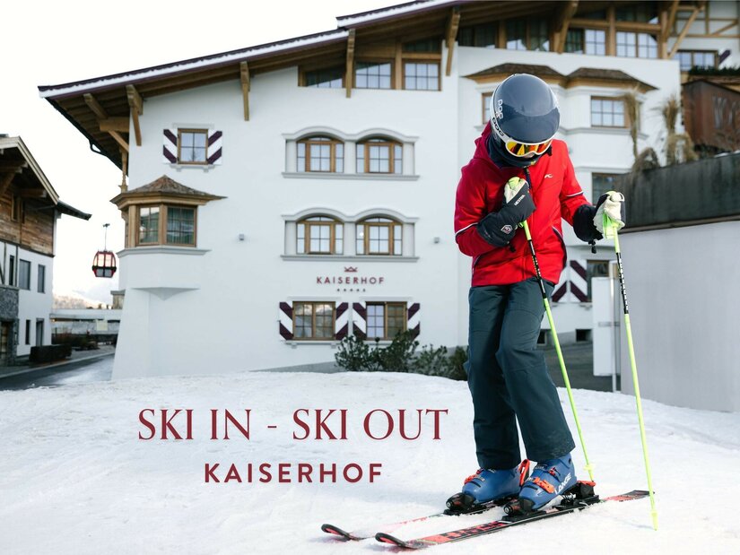 Ein Kind in Skiausrüstung steht auf einer Schneefläche vor dem Hotel Kaiserhof in Kitzbühel.
