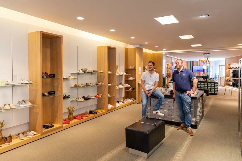 Etz Mode-Sport-Schuhe Zwei Männer in einem hellen Schuhgeschäft mit Holzregalen und verschiedenen Schuhmodellen.