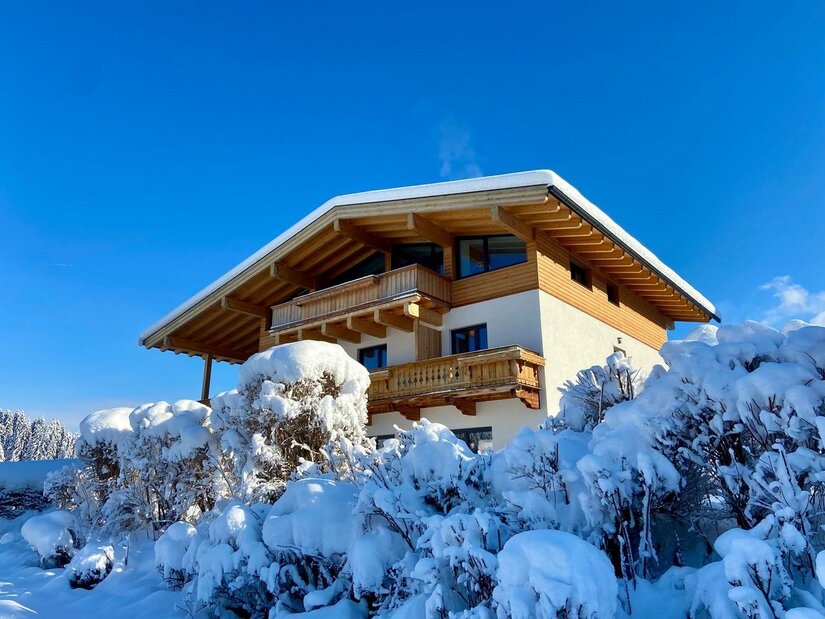 Das Landhaus Barbara im Schnee mit einem klaren blauen Himmel. Umgeben von schneebedeckten Büschen und winterlicher Landschaft.