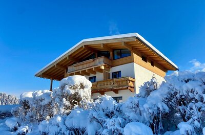 Das Landhaus Barbara im Schnee mit einem klaren blauen Himmel. Umgeben von schneebedeckten Büschen und winterlicher Landschaft.