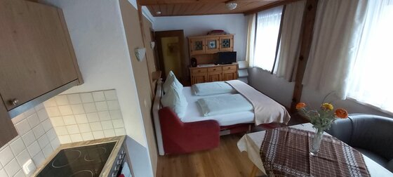 Wohn- und Schlafbereich mit Doppelbett, Küchenzeile und Esstisch.