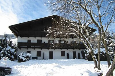 Appartementhaus im Winter Mehrstöckiges weißes Gebäude mit Holzbalkonen in einer verschneiten Winterlandschaft unter blauem Himmel.