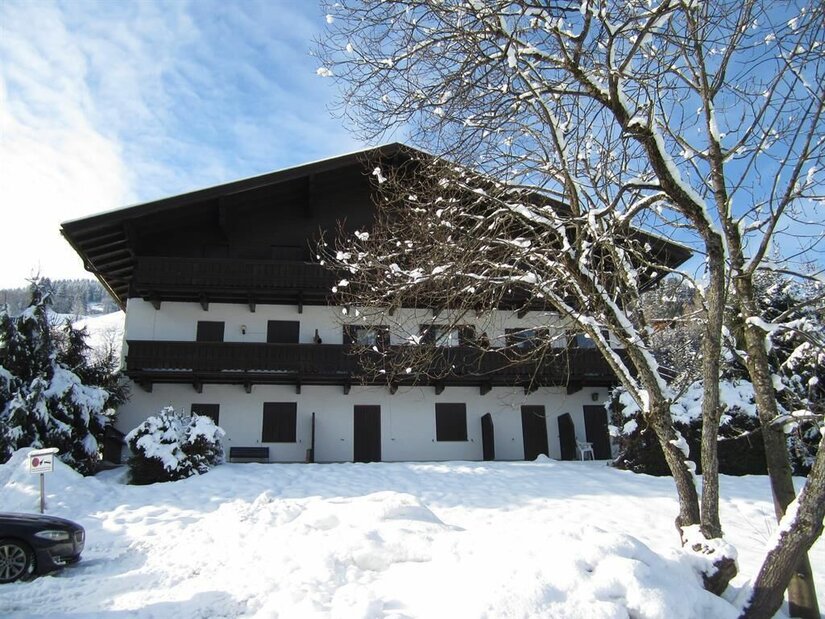 Appartementhaus im Winter Mehrstöckiges weißes Gebäude mit Holzbalkonen in einer verschneiten Winterlandschaft unter blauem Himmel.