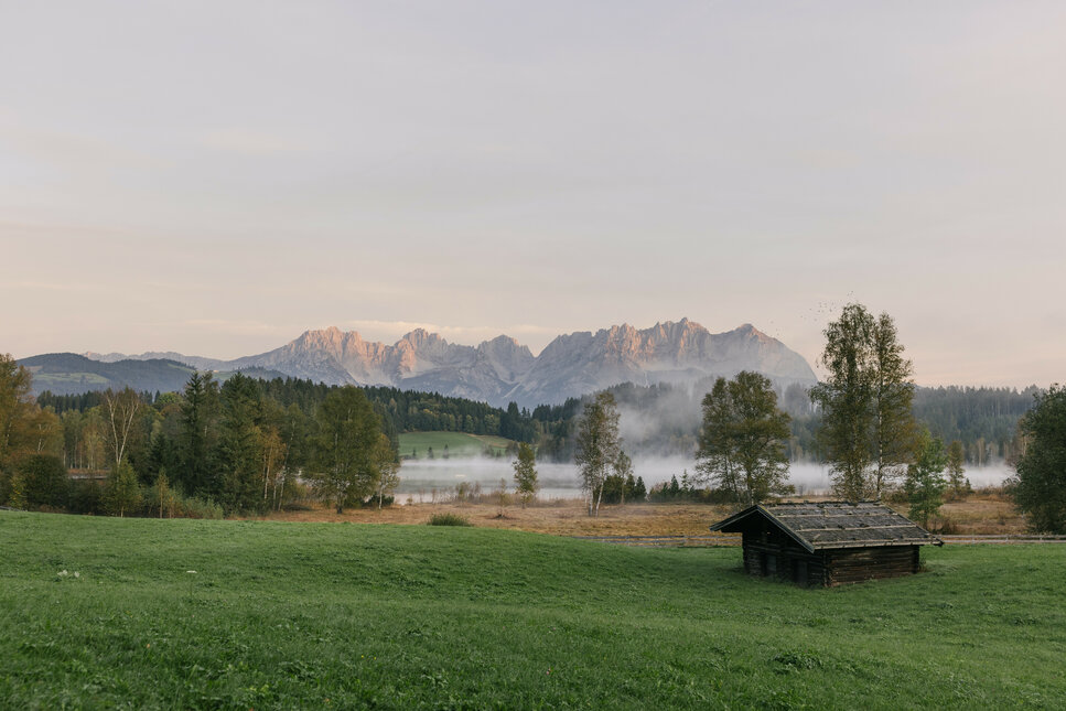 A meadow with a farmhouse in front of Schwarzsee at sunrise