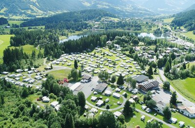 Campingplatz Schwarzsee Luftaufnahme eines Campingplatzes mit Wohnwagen und Zelten an einem See zwischen bewaldeten Hügeln.