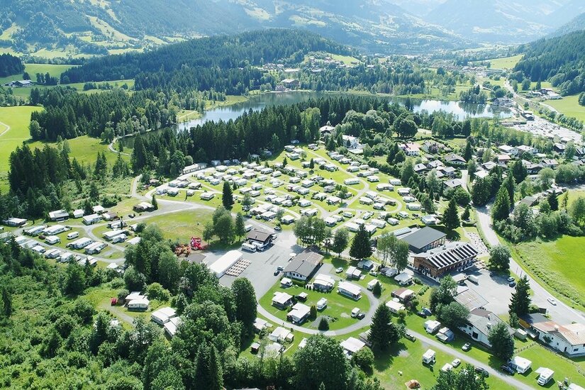 Campingplatz Schwarzsee Luftaufnahme eines Campingplatzes mit Wohnwagen und Zelten an einem See zwischen bewaldeten Hügeln.