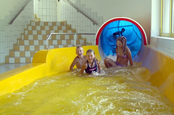 Rutsche Kinder spielen auf einer Wasserrutsche in einem Innenpool. Sie haben Spaß beim Rutschen und Spritzen im Wasser.
