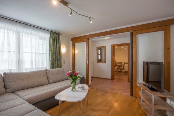 Wohnzimmer mit grauem Ecksofa, hellem Couchtisch und Fernseher vor einer hölzernen Schiebetür.