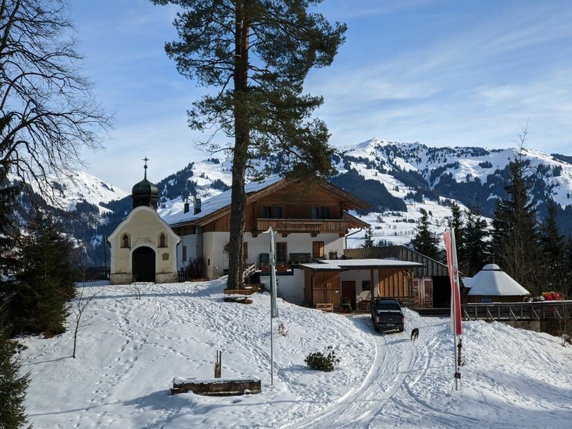Kleine Kapelle und ein alpines Gasthaus in einer verschneiten Berglandschaft mit Nadelbäumen.