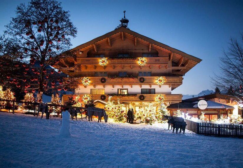 Beleuchtetes Holzgebäude bei Nacht mit Weihnachtsdekoration, Lichterketten und Schneefläche im Vordergrund.