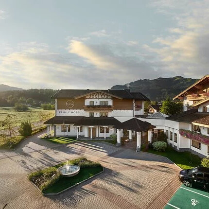 Ein malerisches Familienhotel mit traditioneller Architektur, umgeben von sanften Hügeln und einer grünen Landschaft.