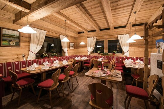 Innenansicht Restaurant Anna Rustikaler Gastraum mit Holzwänden, eingedeckten Tischen und roten Sitzpolstern.