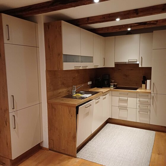 Küche im Haus Huber Moderne Einbauküche in L-Form mit hellen Fronten, Holzdekor-Arbeitsplatte und dunklen Deckenbalken.