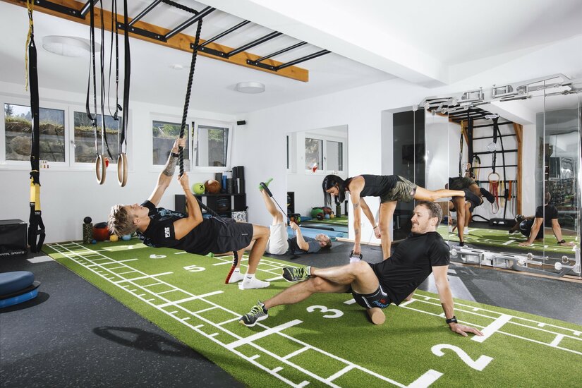 Training bei Sportscare Mehrere Personen trainieren in einem modernen Fitnessraum mit Kunstrasen, Seilen und Hanteln.
