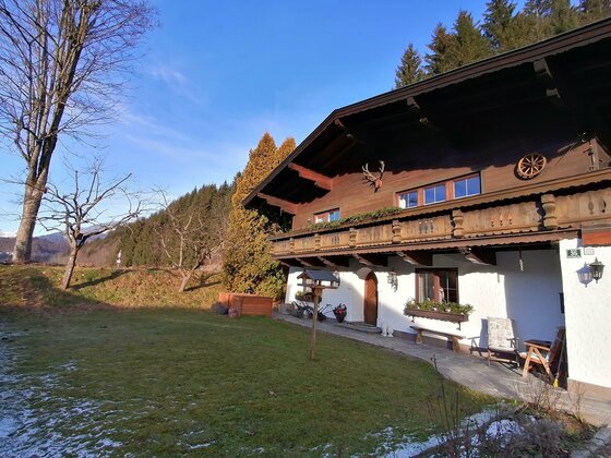 Seitenansicht App. Barbara Alpines Wohnhaus mit dunkler Holzfassade, Balkon und weißem Erdgeschoss vor Waldhintergrund.