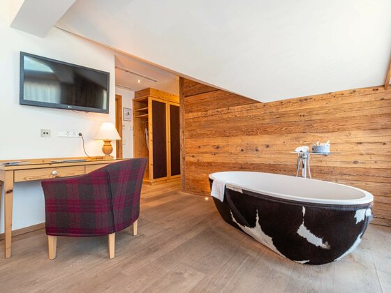 Honeymoon-Suite im Kaiserhof Modernes Hotelzimmer mit freistehender Badewanne in Felloptik, Holzwand und Schreibtisch.