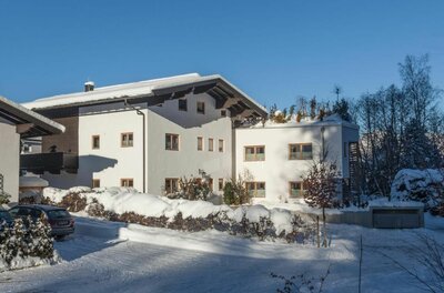 Weißes, mehrstöckiges Alpenhaus mit schneebedecktem Satteldach unter blauem Himmel im Winter.