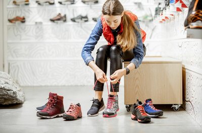 Schuhberatung bei Hervis Eine Frau sitzt in einem Sportgeschäft und schnürt einen grauen Wanderschuh mit pinken Akzenten.