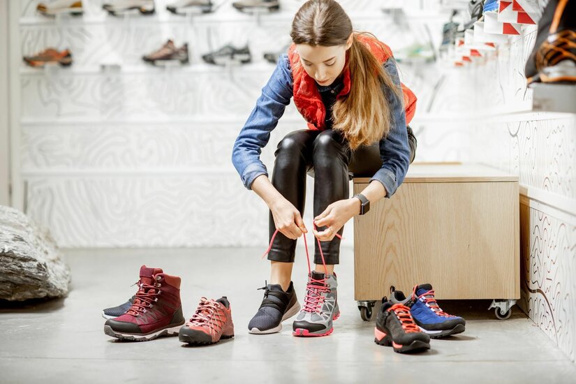 Schuhberatung bei Hervis Eine Frau sitzt in einem Sportgeschäft und schnürt einen grauen Wanderschuh mit pinken Akzenten.