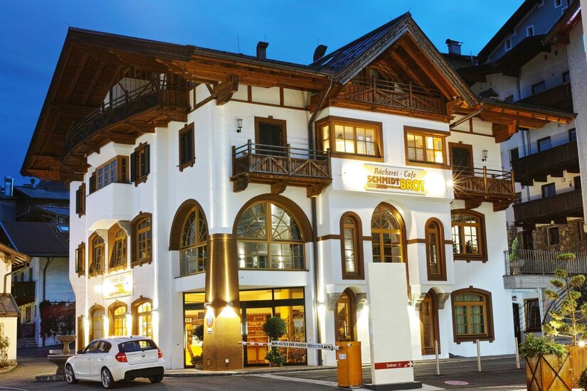 Bäckerei Schmidt Verkauf Beleuchtetes Gebäude der Bäckerei Schmidt mit Holzfassade und Balkonen bei Dämmerung.