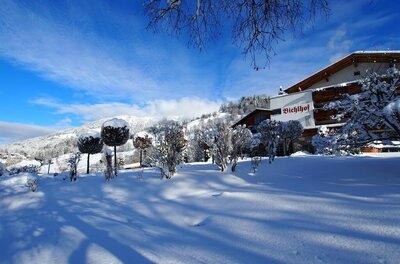Bichlhof Außenaufnahme im Winter Verschneite Gartenanlage vor dem Hotel Bichlhof mit Bergen im Hintergrund unter blauem Himmel.