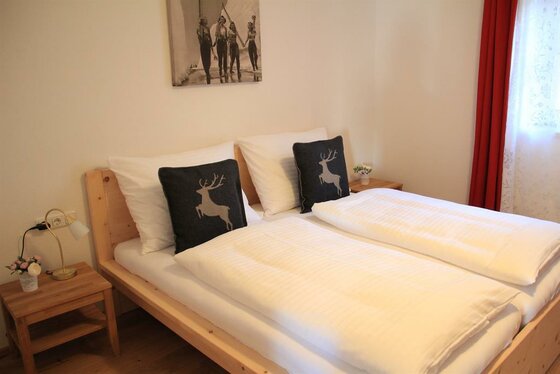 Schlafzimmer im Künstlhäusl Doppelbett aus hellem Holz mit weißer Bettwäsche und dunklen Kissen mit Hirschmotiv.