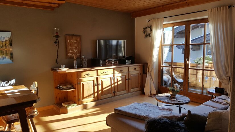 Wohnbereich Ferienwohnung Wielemans Wohnzimmer mit Holzmöbeln, Sofa, Fernseher und Balkonzugang.