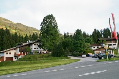 Außenansicht des Gasthofs Jodlbühel mit Parkplatz und bewaldetem Berghang im Hintergrund.