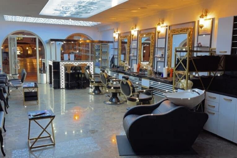 Innenansicht eines modern eingerichteten Barbershops mit goldenen Spiegeln und schwarzen Friseurstühlen.