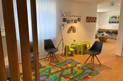Wartezimmer Dr. Petra Hengl Wartebereich einer Praxis mit Spielecke für Kinder, bunten Teppich und modernen Sitzmöbeln.
