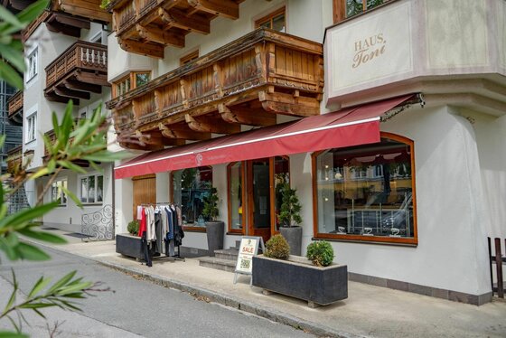 Eingangsbereich eines Bekleidungsgeschäfts mit roter Markise und Holzbalkon darüber.