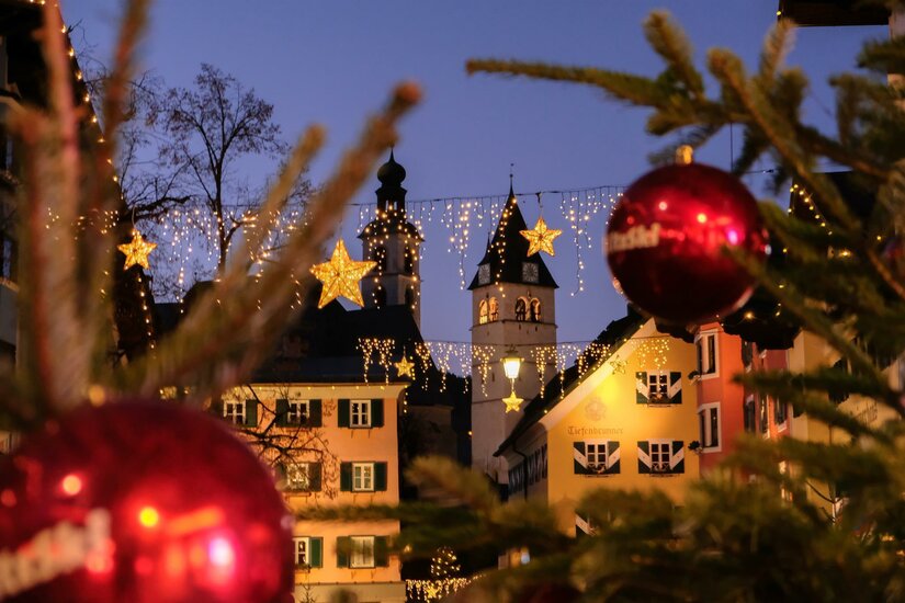 Blick auf beleuchtete Häuserfassaden und Kirchtürme in Kitzbühel mit Weihnachtsdekoration im Vordergrund.