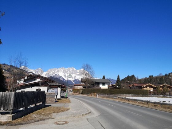 Asphaltierte Straße in einer Siedlung mit Blick auf schneebedeckte Berggipfel unter blauem Himmel.