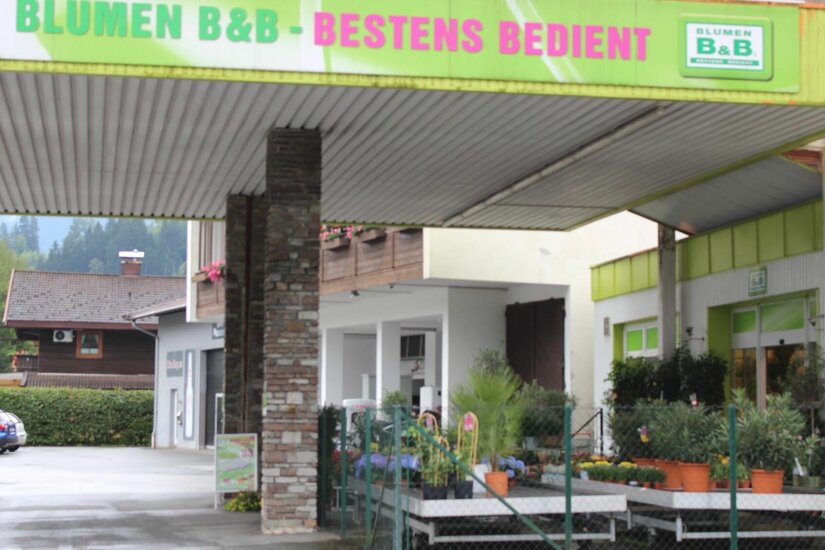 Blumen B&B Geschäft Außenansicht eines Blumengeschäfts mit überdachtem Vorplatz und ausgestellten Pflanzen in Töpfen.