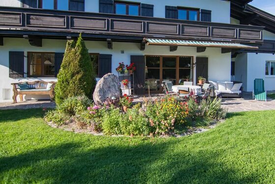 Terrasse Landhaus Gasteiger Terrasse eines Landhauses mit Gartenmöbeln, Blumenbeet und Rasenfläche.