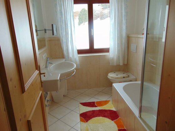 Badezimmer mit Waschbecken, WC, Badewanne und Fenster mit Blick auf verschneite Bäume.