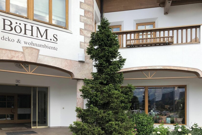 Böhm.s Deko & Wohnambiente Eingangsbereich des Geschäfts Böhm.s mit Nadelbaum und Holzfassade.