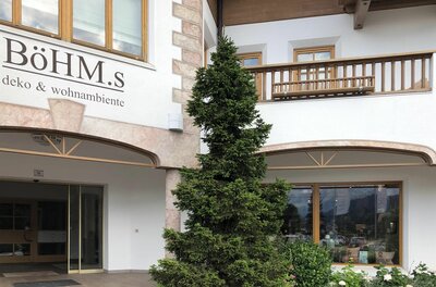 Böhm.s Deko & Wohnambiente Eingangsbereich des Geschäfts Böhm.s mit Nadelbaum und Holzfassade.