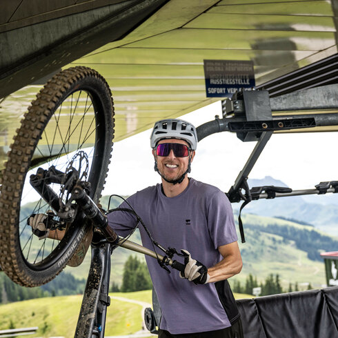 Ein Mountainbiker nimmt sein Fahrrad an einer Liftstation der 360 Flow Trails Kitzbühel vom Bike-Lift, lächelnd und bereit für die nächste Abfahrt.
