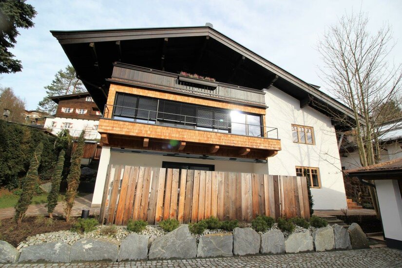 Modernes Alpenhaus mit Holzfassade, Balkon und Steingarten.