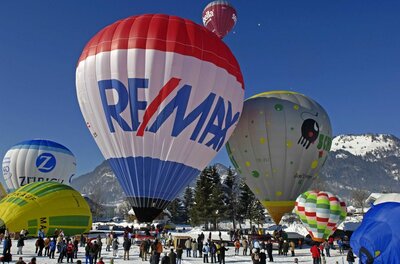 Ballonfahren in Tirol Mehrere bunte Heißluftballons starten von einer verschneiten Fläche vor einer Bergkulisse.