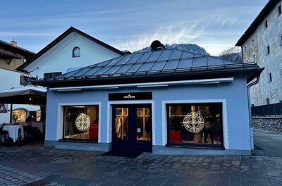 Außenansicht eines Stone Island Ladengeschäfts in einem hellblauen Gebäude mit Bergpanorama im Hintergrund.