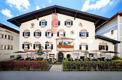 Ein charmantes Hotelgebäude mit traditioneller bayerischer Architektur. Es hat viele Fenster und eine einladende Terrasse im Freien.
