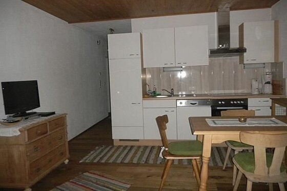 Wohnküche im Seiwaldhof Brandstätter Kombinierter Wohn- und Essbereich mit weißer Küchenzeile, Holztisch und Fernseher auf einer Kommode.