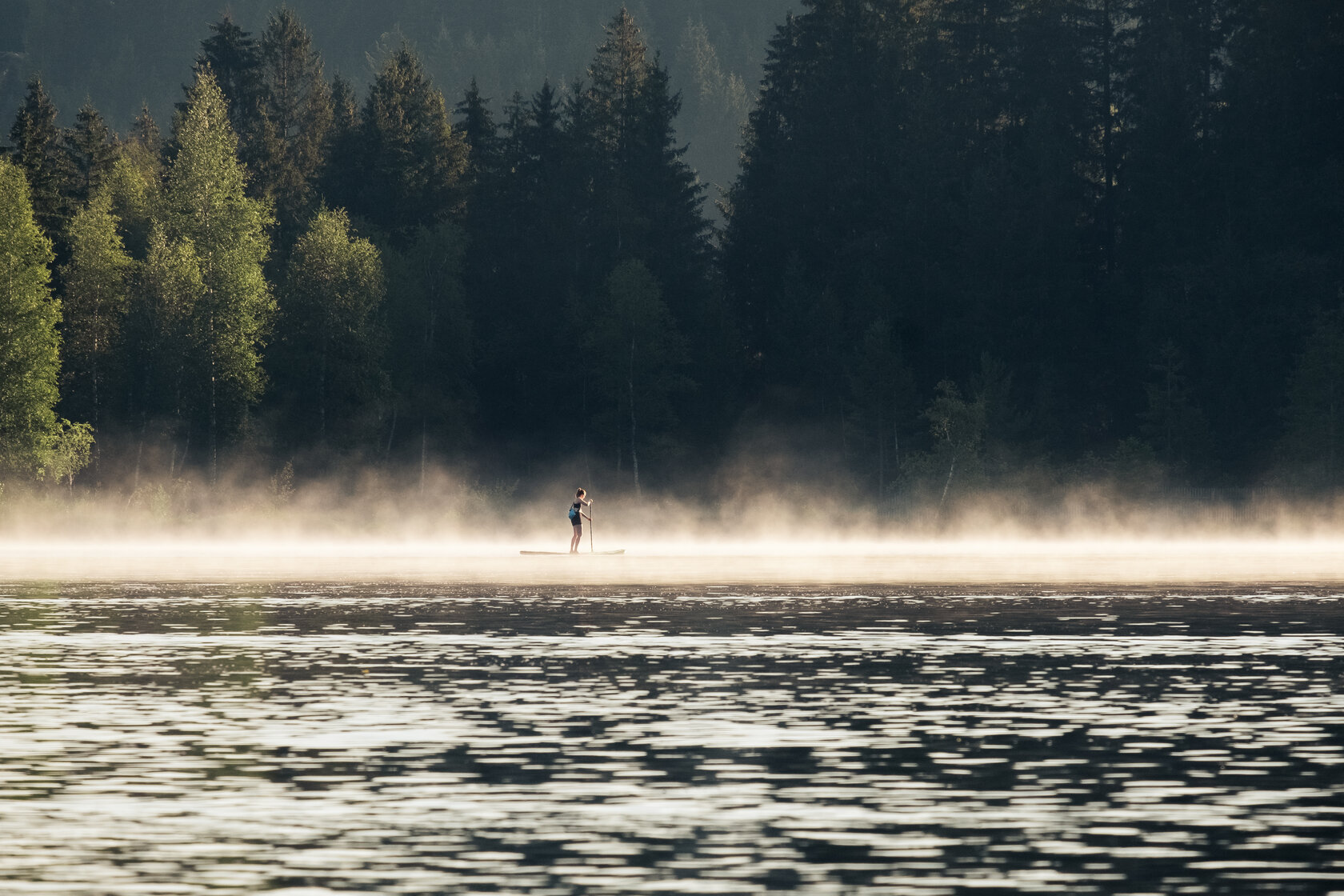 Der Schwarzsee mit einer zarten Nebelschicht über der Wasseroberfläche und einem Paddler auf seinem SUP